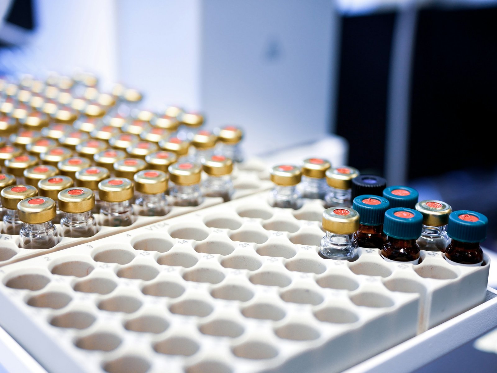 Laboratory sample vials with gold and blue caps arranged in an instrument tray